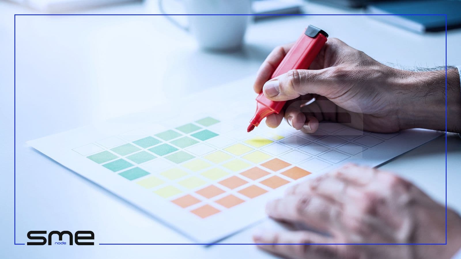 Hands colouring the cells of a printed grid with highlighters, green and yellow in one corner and orange toward the other, scoring risks by likelihood and impact