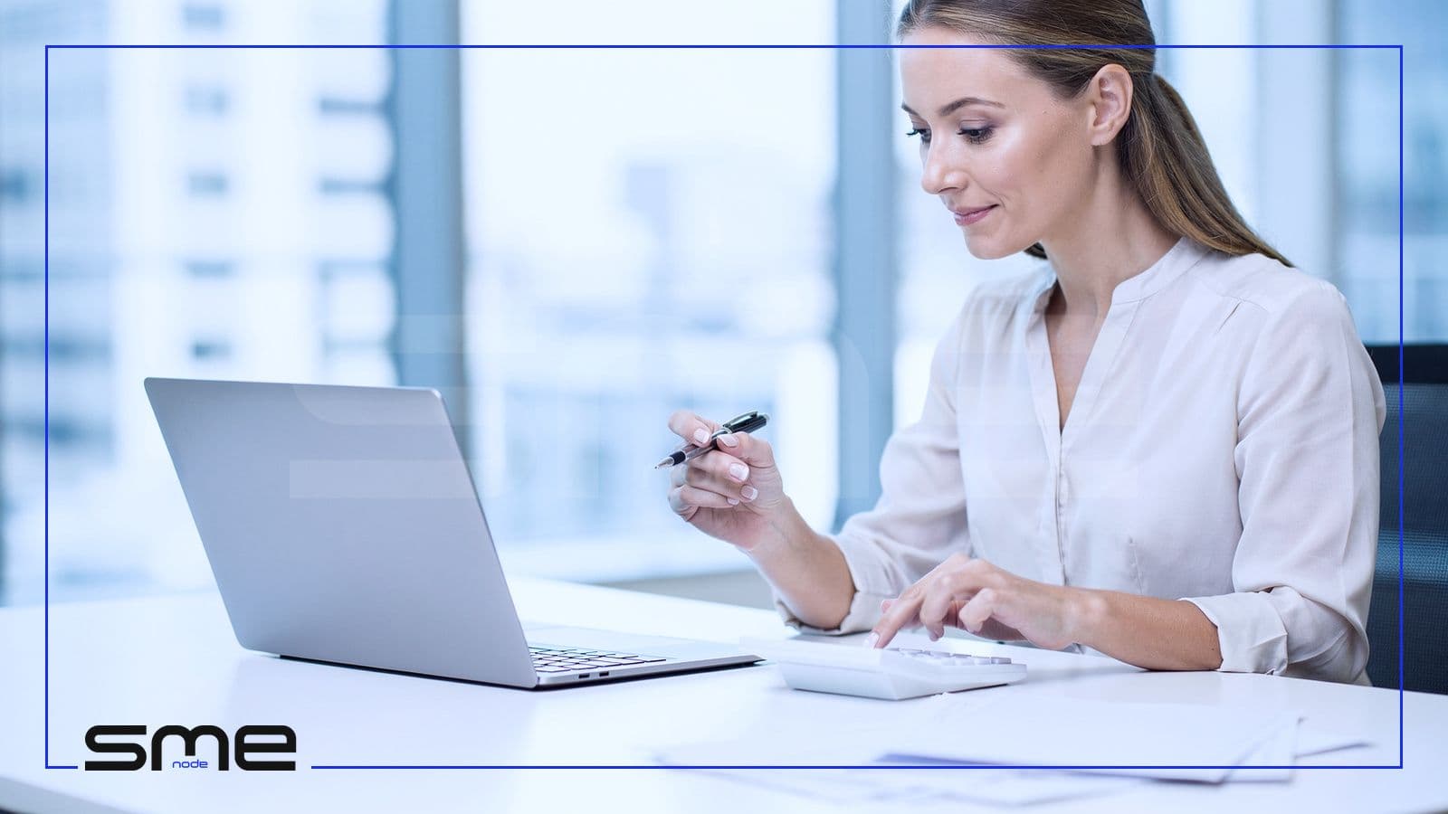 A finance manager at a bright office desk adding up monthly costs on a calculator next to her laptop