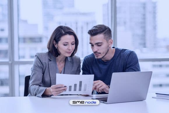 An IT manager and a cloud engineer reviewing a printed monthly cloud cost report beside a laptop in a bright Toronto office
