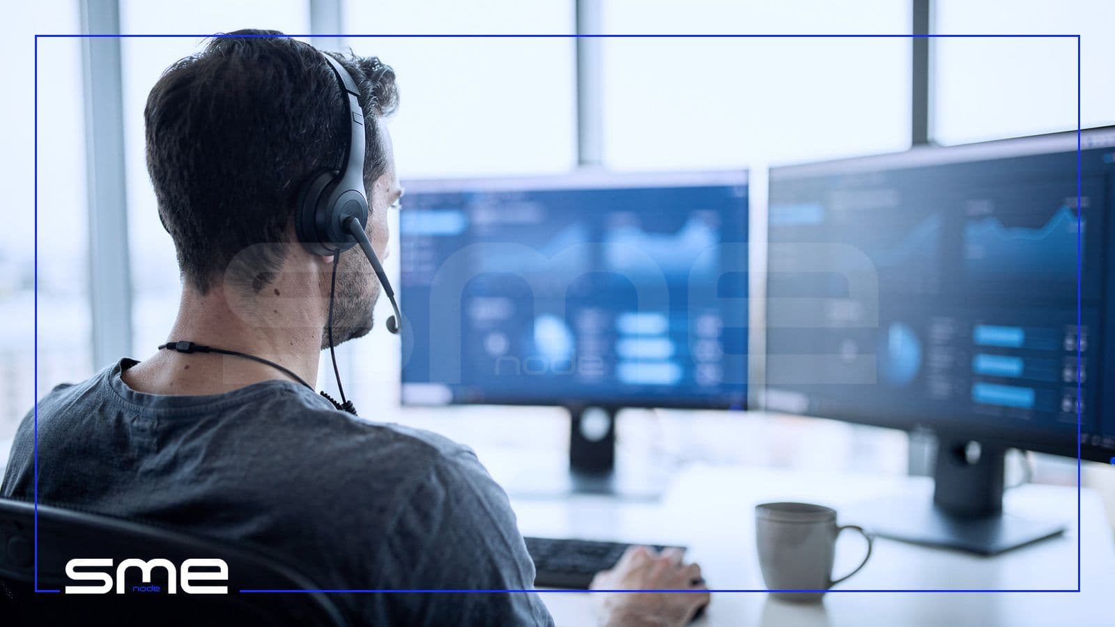 A cloud operations engineer with a headset watching monitoring dashboards on two screens in a bright operations room