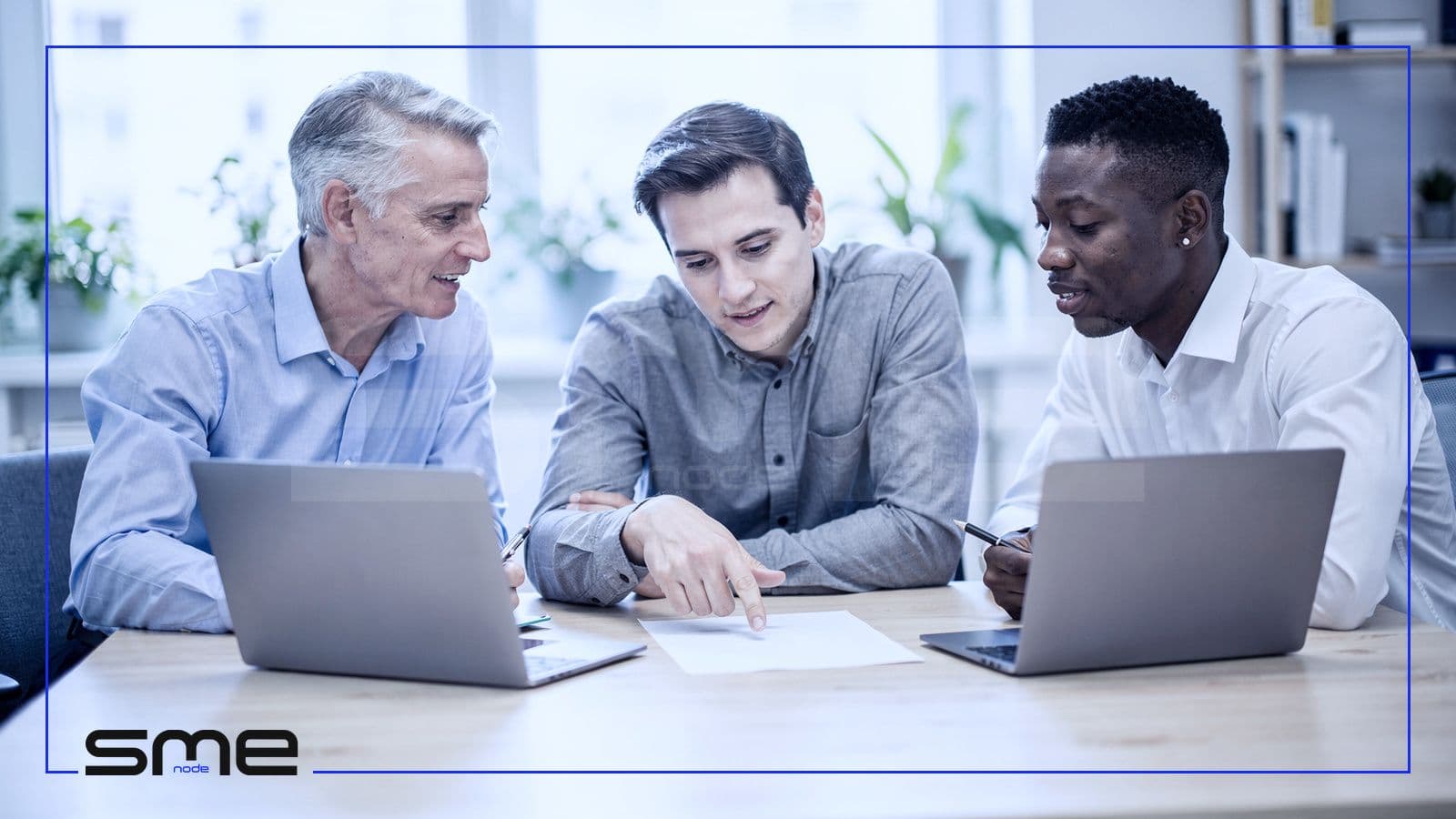 Three colleagues at a shared table with two laptops reviewing a document together, the kind of file work that can move to the cloud