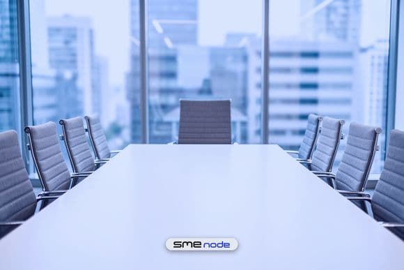 An empty boardroom with grey chairs tucked in along a long white table and the seat at the head left open, the place a part-time CIO fills