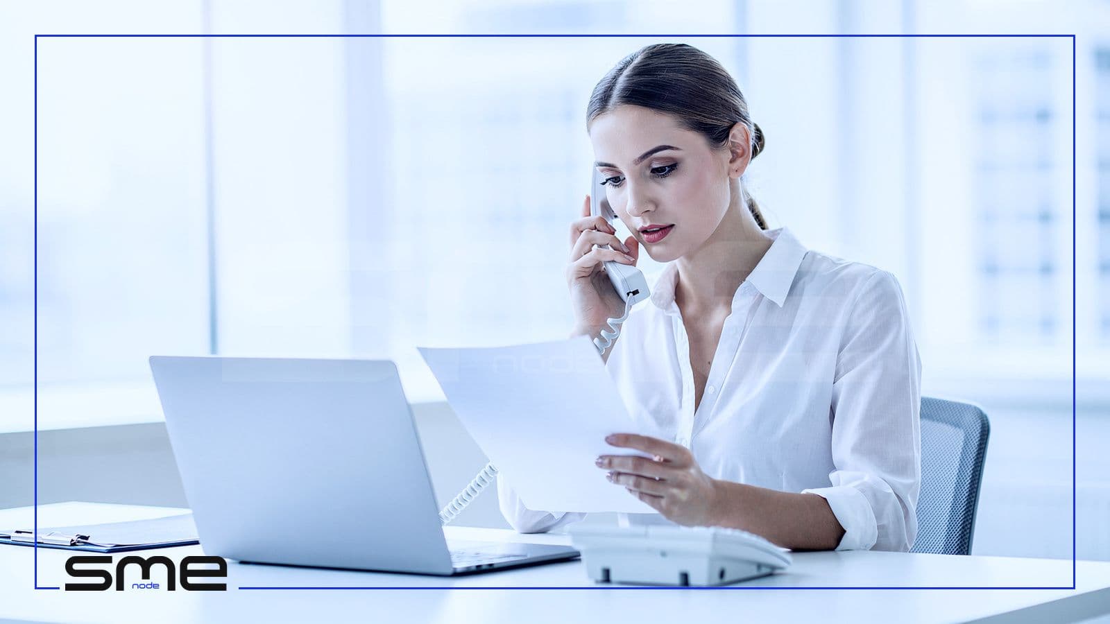 A help desk technician on a desk phone checking a printed sheet while calling a user back to verify identity