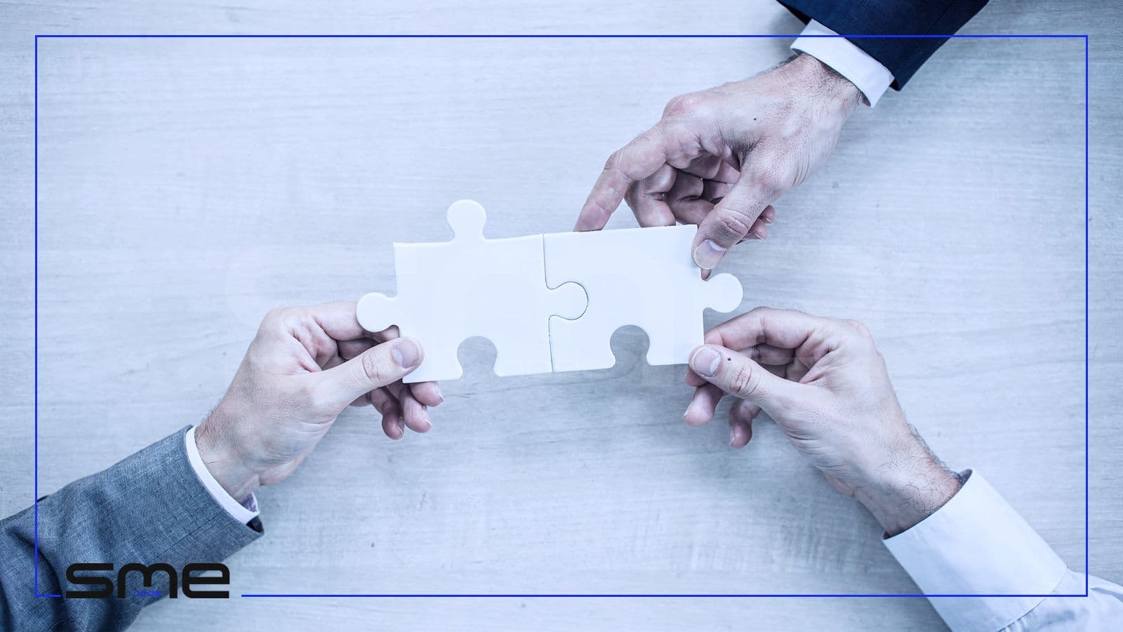 Three hands reaching in from three sides to join white jigsaw pieces on a light table, a picture of governance, risk and compliance working as one programme
