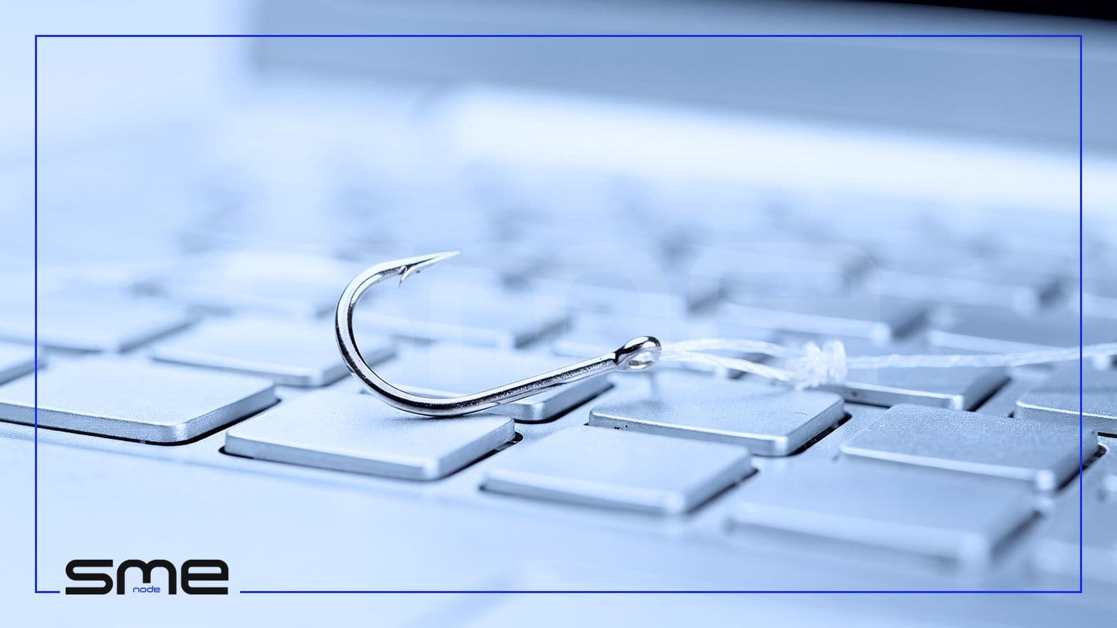 A steel fishing hook with a short line lying on a silver laptop keyboard, a picture of phishing and invoice fraud, the most common cyber risk Canadian businesses report