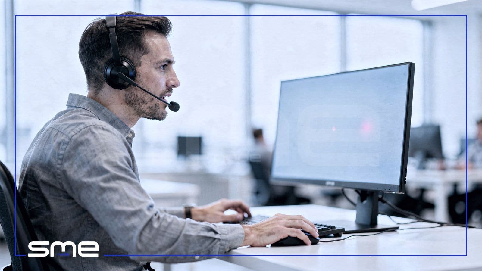 Security analyst wearing a headset talking on a call while monitoring his screen in a bright office