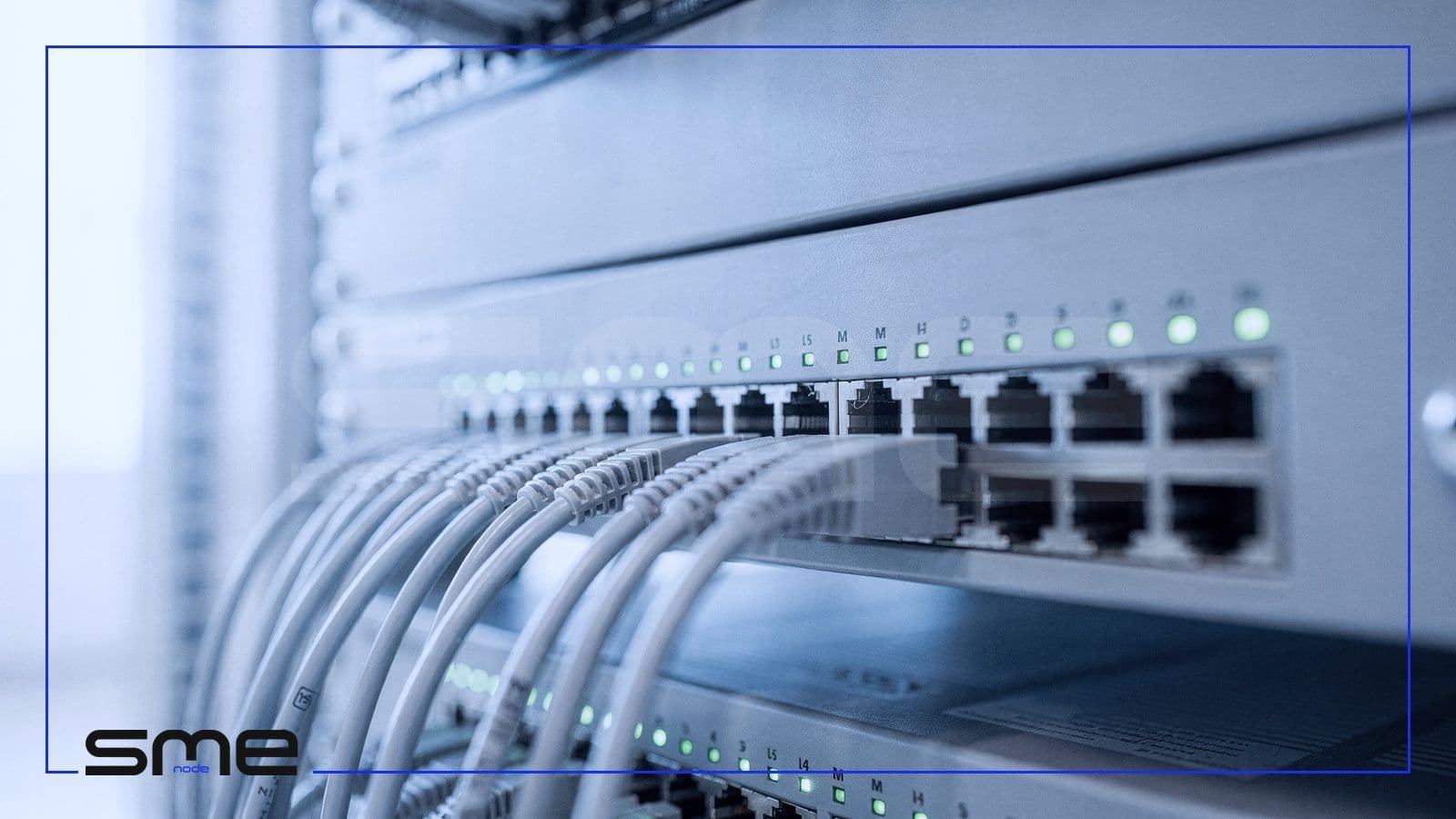 Close-up of a network switch and firewall with grey patch cables and green status lights in a server rack