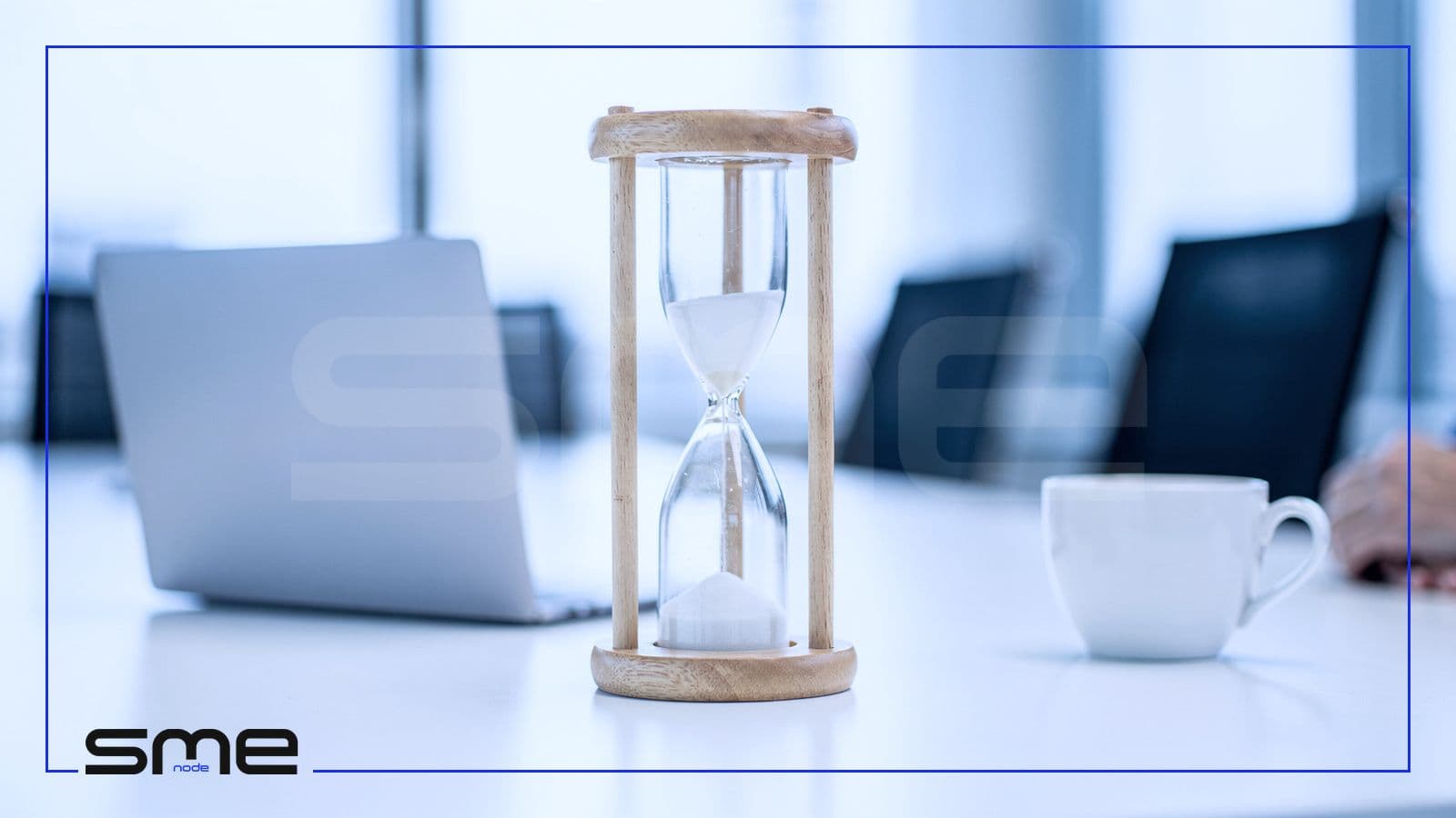 A wooden hourglass half run through on a meeting table beside a laptop and a coffee cup, standing for how much CIO time a business needs