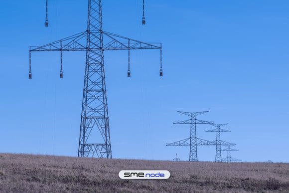 High-voltage transmission towers in a line across a dry field under a clear blue sky, the kind of interprovincial power line system Bill C-8 lists as critical infrastructure