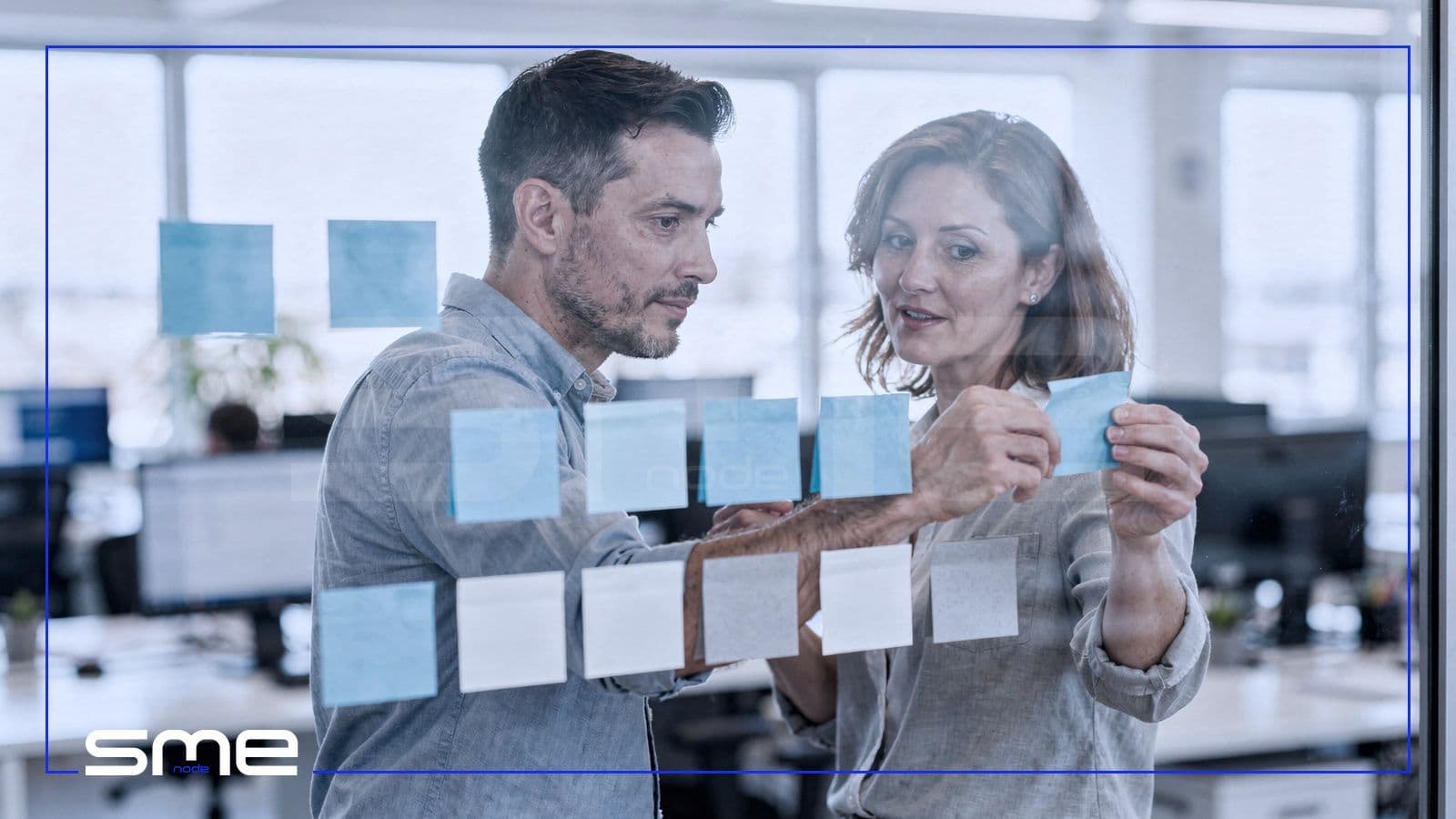Two IT professionals arranging blank sticky notes in rows across a glass wall to plan an IT roadmap by quarter