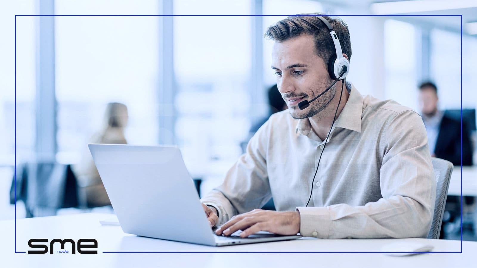 An IT service desk technician wearing a headset reviewing a ticket on a laptop in a bright office