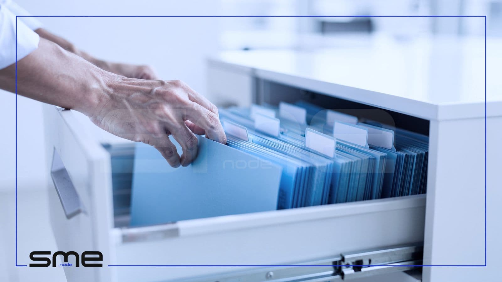 Hands filing pale blue folders into an open filing cabinet drawer, the evidence a company collects before its own SOC 2 Type 2 examination